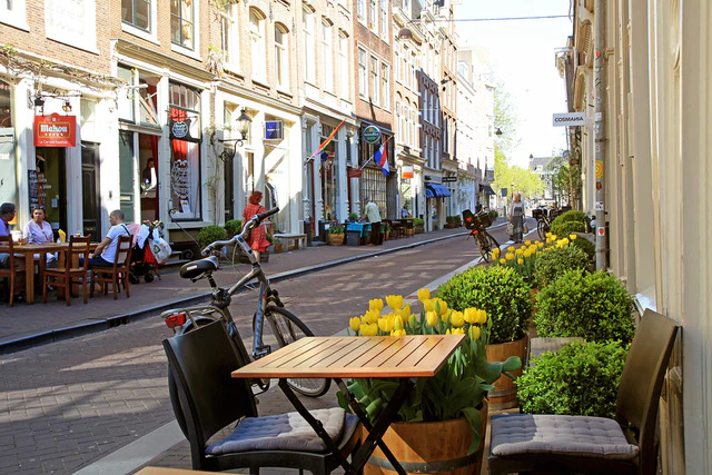 Uitnodigend buitenterras van een café in het winkelgebied van de Negen Straatjes in Amsterdam, met levendige tulpen en voorbijgangers.