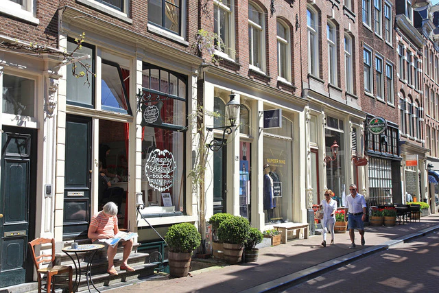 Gezellige straatbeeld van Hotel IX Amsterdam in de Negen Straatjes buurt met gasten die genieten van het zonnige weer.